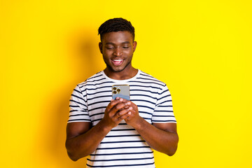 Portrait of nice young man use smart phone wear striped t-shirt isolated on vibrant yellow color...