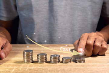 A man points at a stack of coins with a down arrow. Cost reduction concept.