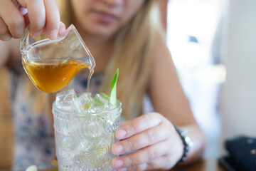 Asian woman pouring honey to mixing cocktail mocktail cold drink into the drinking glass on ice lemon tea to refreshing relieve fatigue