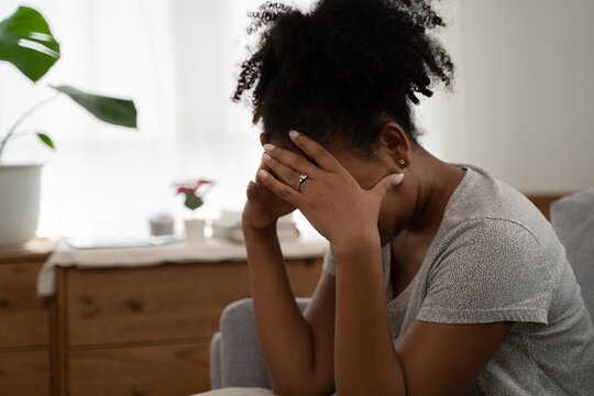 Depressed lonely unhappy mental woman sitting and crying alone on the sofa at home with hand on face feel down stress sad and worried disappoint while facing heartbreak problem or migraine headache