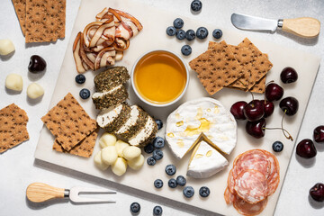 Cheese and ham marble platter. Assorted cheeses, honey, salami, berries and bread crackers on white marble board
