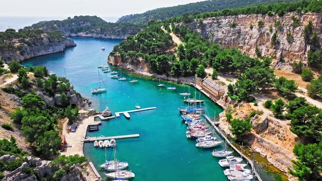 Aerial view of a long, narrow inlet featuring a marina lined with sailboats and hiking path with scenic water views. Calanque de Port-Miou in the eastern calanque between Marseille and Cassis.
