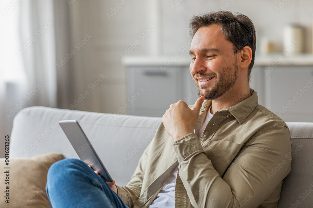 Aufkleber a man is sitting on a white couch in a living room, using a tablet. he is dressed in a tan button do