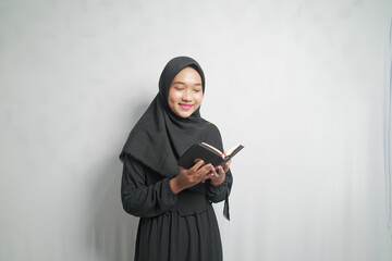 A Muslim woman in a black hijab reading a Quran