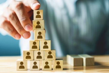 Building a Strong Team: A strategic hand assembles a pyramid of wooden blocks, each bearing the symbol of a person, representing the concept of team building and organizational growth. 