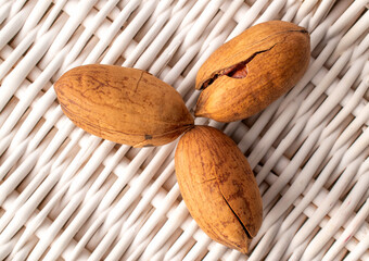 Three unshelled pecan nuts on vine mat, macro, top view.