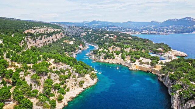 Aerial view of Tourist attraction beach, people enjoying summer vacation in Parc du Mugel, France. Snug Cove framed by rugged cliffs, with calm swimming off a pebble beach, and turquoise clear water.