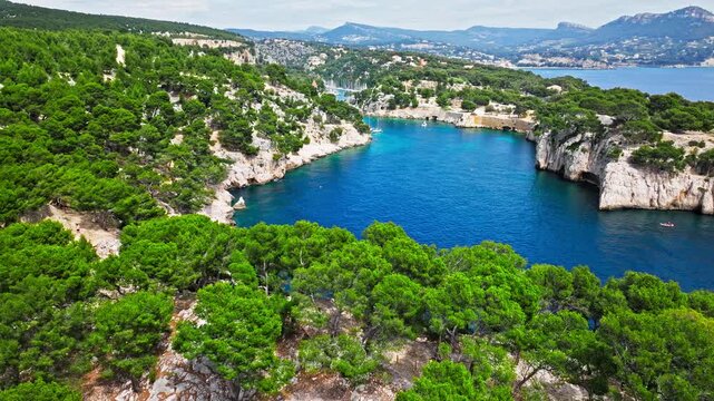 Aerial view of Tourist attraction beach, people enjoying summer vacation in Parc du Mugel, France. Snug Cove framed by rugged cliffs, with calm swimming off a pebble beach, and turquoise clear water.