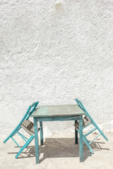 A tranquil moment captured with two wooden chairs and a small table, inviting relaxation against a whitewashed wall in the picturesque Cyclades.