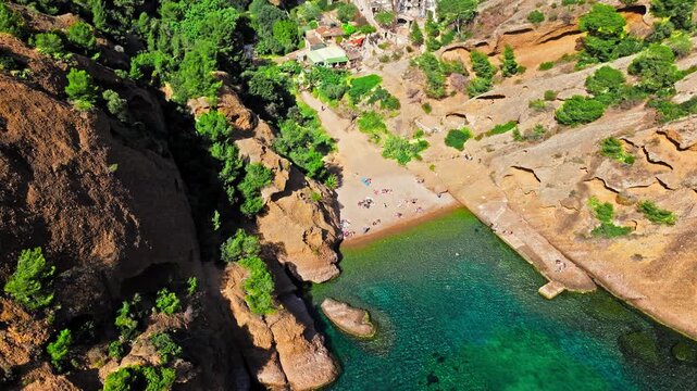 Aerial view of Tourist attraction beach, people enjoying summer vacation in Parc du Mugel, France. Snug Cove framed by rugged cliffs, with calm swimming off a pebble beach, and turquoise clear water.