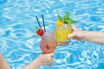 Mother with her little girl at swimming pool drinking healthy refreshing juices. Relaxing summer vacation concept