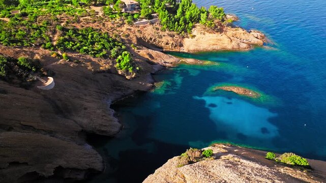 Aerial view of a Botanical garden with Snug Cove framed by rugged cliffs in Parc du Mugel. View from above of swimming off a pebble beach with turquoise clear water in France.