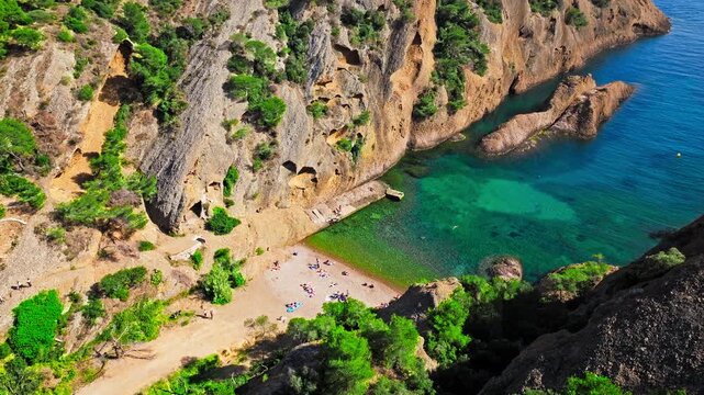 Aerial view of Tourist attraction beach, people enjoying summer vacation in Parc du Mugel, France. Snug Cove framed by rugged cliffs, with calm swimming off a pebble beach, and turquoise clear water.