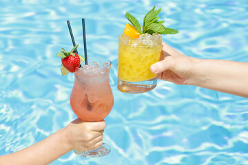 Mother with her little girl at swimming pool drinking healthy refreshing juices. Relaxing summer vacation concept