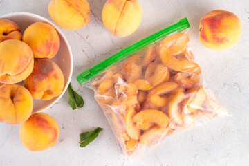 Frozen peaches in freezing bags with fresh ripe raw peach fruits on kitchen white table, Healthy simple canning, freezing stock up of fruit harvest for winter concept. 