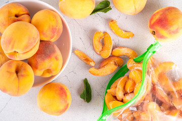 Frozen peaches in freezing bags with fresh ripe raw peach fruits on kitchen white table, Healthy simple canning, freezing stock up of fruit harvest for winter concept. 