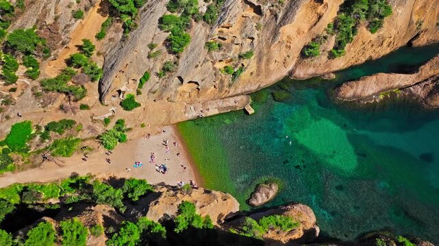 Aerial view of Tourist attraction beach, people enjoying summer vacation in Parc du Mugel, France. Snug Cove framed by rugged cliffs, with calm swimming off a pebble beach, and turquoise clear water.