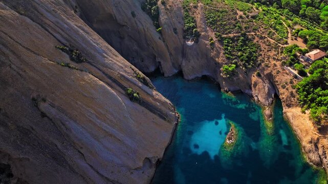 Aerial view of a Botanical garden with Snug Cove framed by rugged cliffs in Parc du Mugel. View from above of swimming off a pebble beach with turquoise clear water in France.