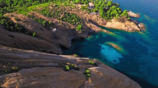 Aerial view of a Botanical garden with Snug Cove framed by rugged cliffs in Parc du Mugel. View from above of swimming off a pebble beach with turquoise clear water in France.