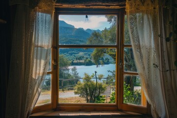 A window with a view of a lake and mountains. The curtains are white and the window is open