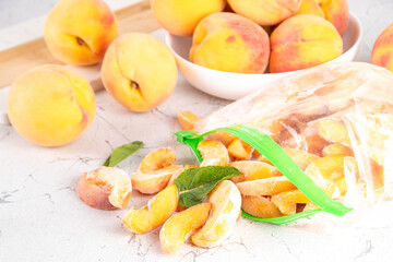 Frozen peaches in freezing bags with fresh ripe raw peach fruits on kitchen white table, Healthy simple canning, freezing stock up of fruit harvest for winter concept. 