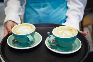 A barista is skillfully making lattes in green cups and serving them at a cozy cafe