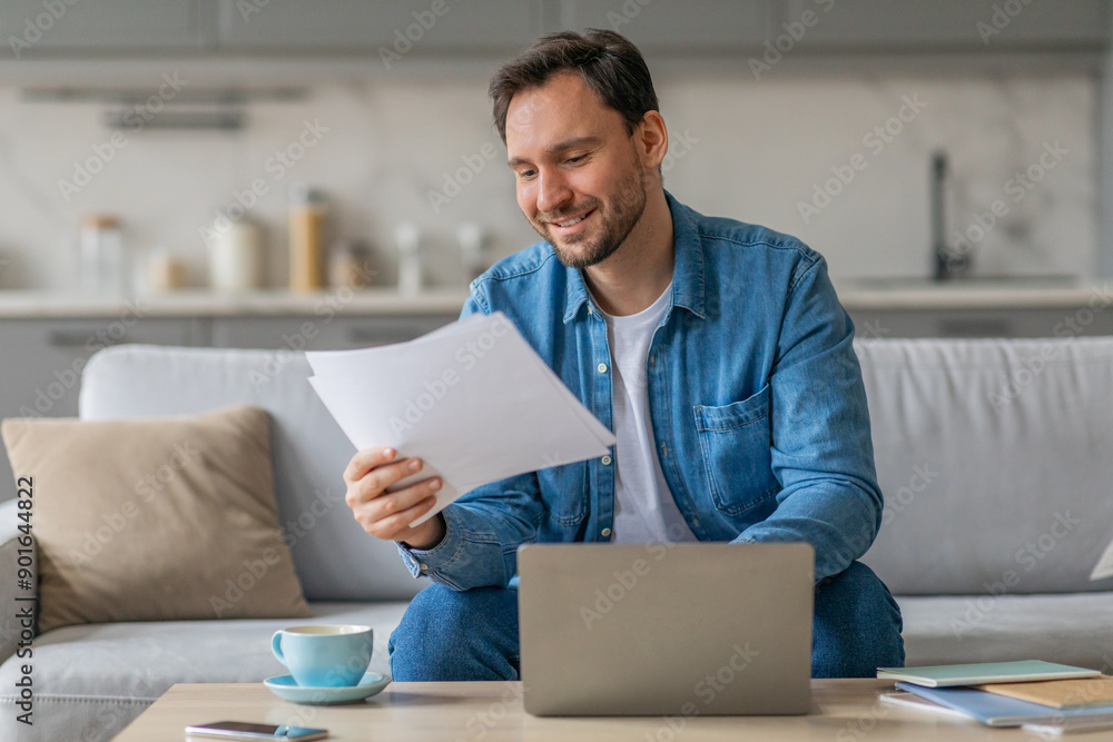 Aufkleber a man in a blue shirt sits on a couch, reviewing documents while working on his laptop. a cup of cof