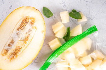 Frozen melon slices, cubes in freezing bags with fresh ripe raw melon on kitchen white table,...