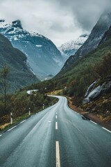 Naklejka premium A long road with a mountain range in the background. The road is wet and the sky is cloudy
