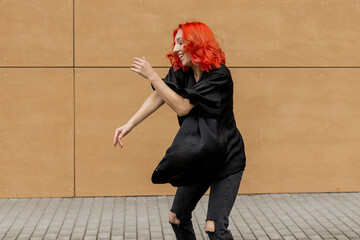 Happy positive emotional dancer curling in dance. Woman with red hair dancing on urban street, on...