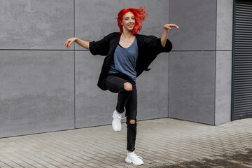 Happy positive emotional dancer curling in dance. Woman with red hair dancing on urban street, on...