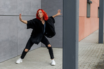 Happy positive emotional dancer curling in dance. Woman with red hair dancing on urban street, on...