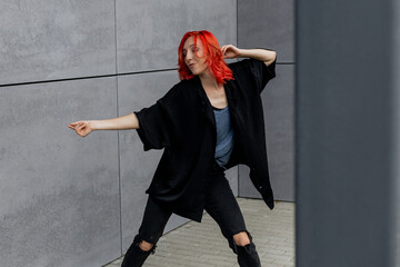 Happy positive emotional dancer curling in dance. Woman with red hair dancing on urban street, on...