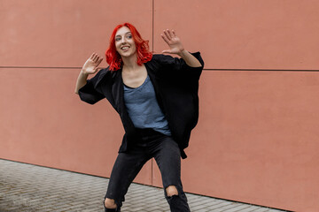 Happy positive dancer curling in dance. Woman with red hair dancing on urban street, on pink wall...