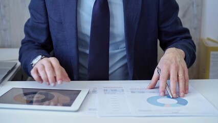 Businessman with blue suit is analyzing financial data using charts and graphs on paper and a tablet. Business and audit