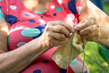 Hands of an elderly woman knitting socks for grandchildren. Pensioner enjoying her hobby in yard on...