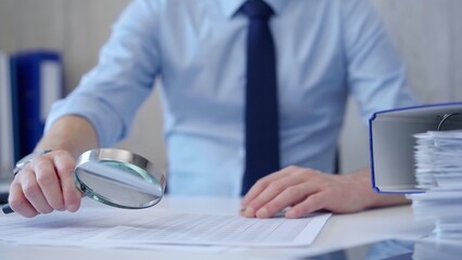 Businessman is carefully examining financial documents with a magnifying glass, highlighting the importance of thorough analysis in business. Audit and taxes