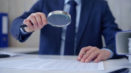Businessman is carefully examining financial documents with a magnifying glass, highlighting the importance of thorough analysis in business. Audit and taxes