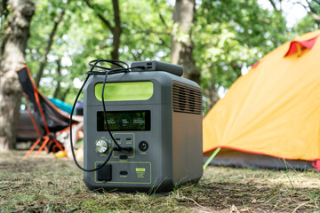 Portable power station with lithium ferrophosphate battery  charging electronic  devices used at a wild camp site,  in front  of yellow tent