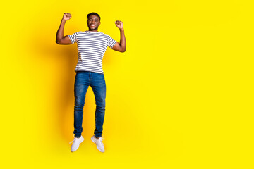 Full size photo of nice young man jump raise fists empty space wear t-shirt isolated on bright yellow color background