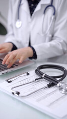 Fototapeta premium Stethoscope is lying on the glass table while doctor woman is working with laptop computer on the background, close-up. Medicine and pharmacy concept
