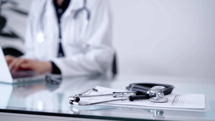 Stethoscope is lying on the glass table while doctor woman is working with laptop computer, horizontal view. Medicine and pharmacy concept