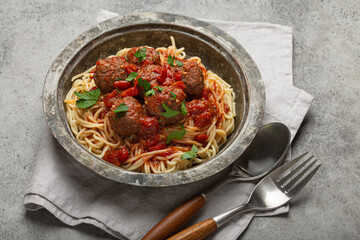 Delicious spaghetti with meatballs and tomato sauce on a rustic table with neatly arranged cutlery and napkin, Italian cuisine