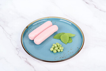 Breakfast with boiled sausages, green peas and basil leaves.