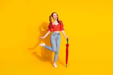 Full body length photo of young lady in red blouse and jeans holding parasol during rainy day spring season isolated on yellow color background © deagreez
