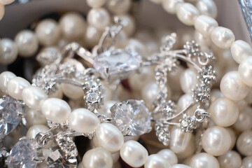 Elegant pearls and silver jewelry with diamonds lie intertwined, reflecting their exquisite...
