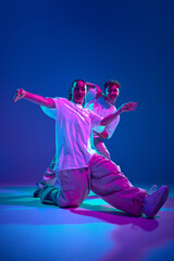 Dynamic image of artistic and energetic young man and woman, dancers performing hip-hop against purple studio background in neon light. Concept of contemporary dance, hobby, youth