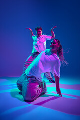 Dynamic performance. Young man and woman, dancers dancing hip-hop, attending contemporary dance show against purple studio background in neon light. Concept of contemporary dance, hobby, youth