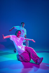 Artistic youth. Dynamic image of talented young girl and guy, hip-hop dancers in motion, performing against purple studio background in neon light. Concept of contemporary dance, hobby, youth