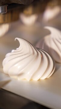 White creamy marshmallows are squeezed on the moving conveyor belt. Close up. Automated line for sweet products manufacturing. Confectionery concept. Vertical video